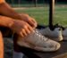 Player unlacing worn padel shoe on bench