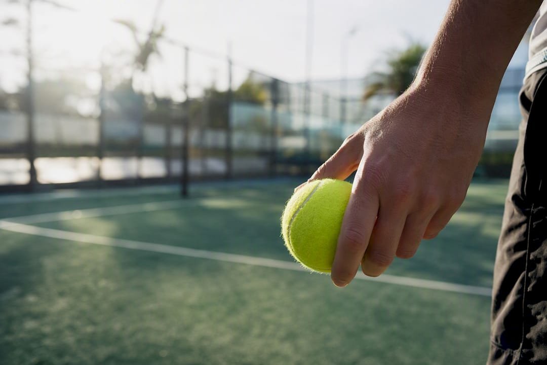 Hand holding padel ball on sunlit outdoor court